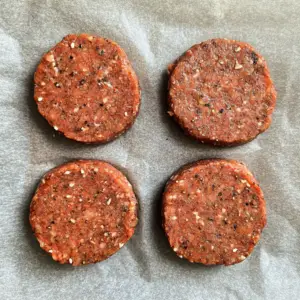 four evenly shaped raw beef patties placed on a parchment-lined surface