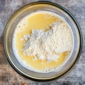 glass mixing bowl containing a frothy mixture of yellow tinted warm milk