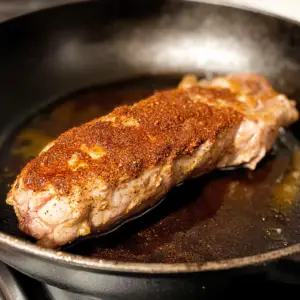 pork tenderloin being seared in a cast-iron skillet