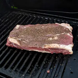 raw beef brisket resting on a black smoker grill