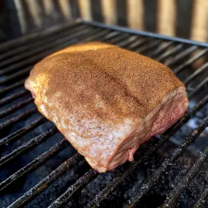 raw brisket point resting on the grates of a smoker