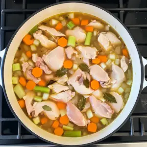 raw chicken pieces submerged in a golden, simmering broth