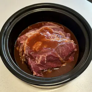 raw chuck roast sits in the center of a slow cooker