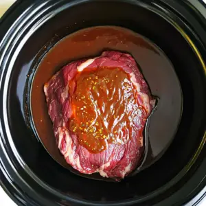 raw chuck roast sitting in the center of a black slow cooker