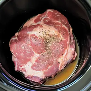 raw pork shoulder sits in the center of a black slow cooker