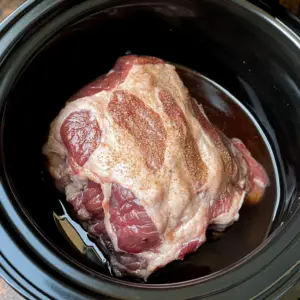 raw pork shoulder sitting in a black slow cooker