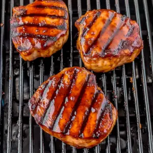 seasoned pork chops sizzling on a hot grill