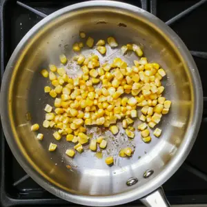 bright yellow corn kernels sizzling in a stainless steel skillet