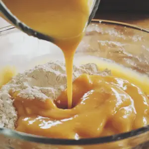 dry flour mixture, with a stream of golden-yellow wet ingredients