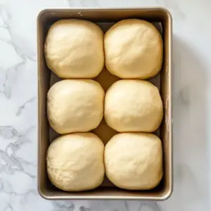 loaf pan containing six smooth, evenly sized balls of brioche dough