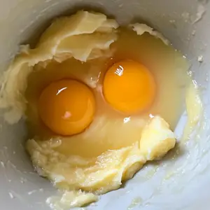 mixing bowl containing two egg yolks, applesauce, melted coconut oil, milk, and vanilla extract