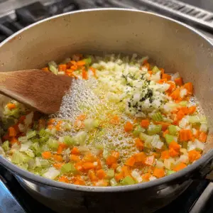 mix of diced onions, celery, and grated carrots is being sautéed