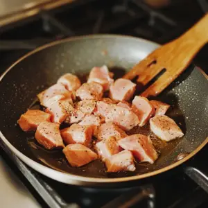 sliced cubes of raw chicken breast are being seared