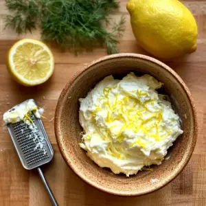 softened cream cheese being mixed with fresh lemon zest and a splash of lemon juice